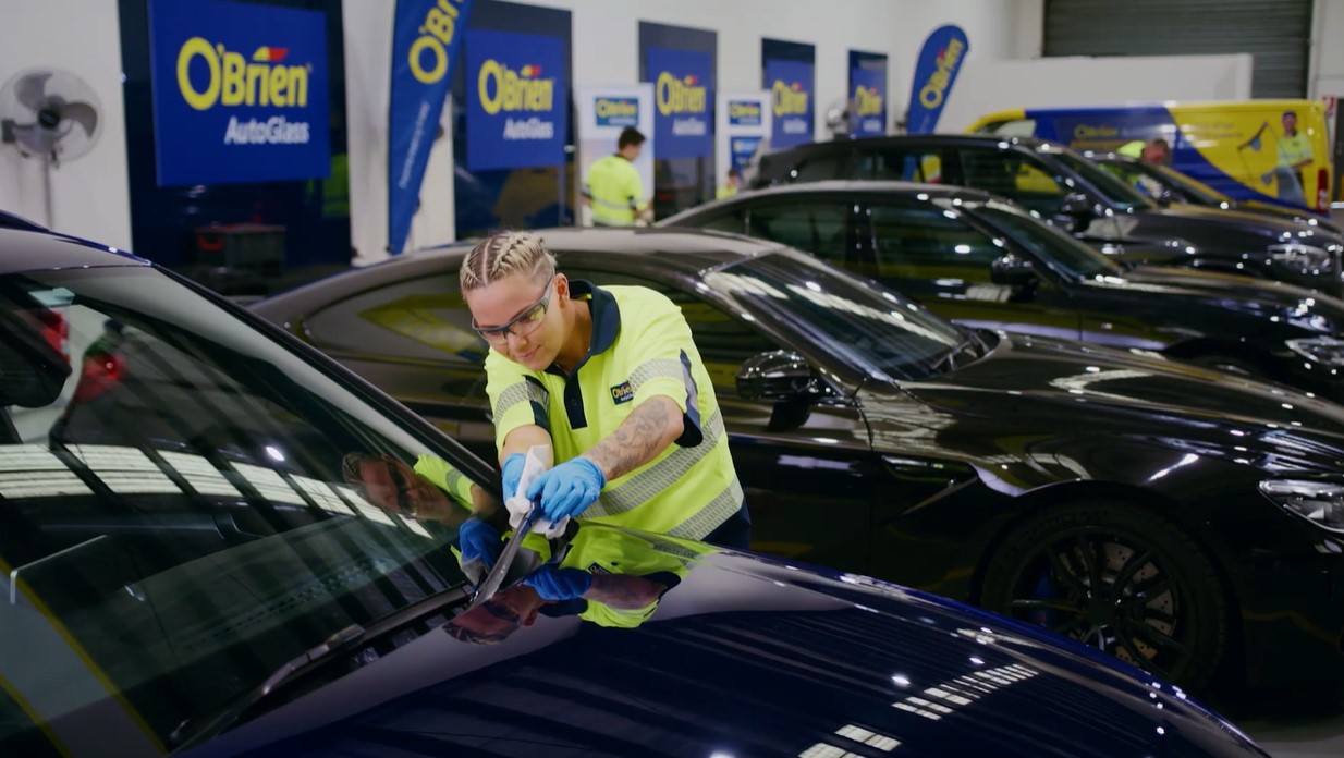 An O'Brien technician is seen inspecting and cleaning the windshield wipers of a vehicle.